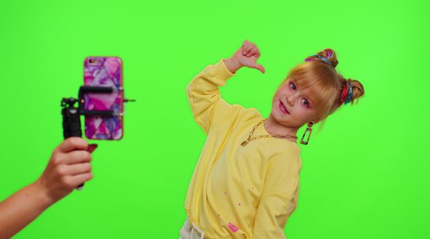 Young Blogger Concept. Cheerful teen school girl kid dancing at camera filming video using phone at home on chroma key background, creating her trendy content on a mobile app to share on social media
