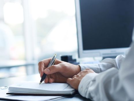 businessman writes in a notebook while sitting at a desk