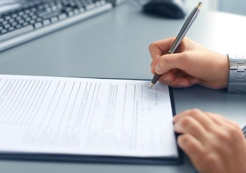 Businesswoman sitting at office desk signing a contract with shallow focus on signature.