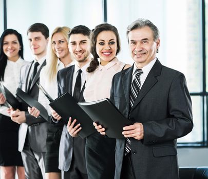 A group of businessmen standing one after another with folders in hands at the office