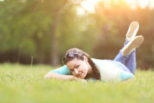 Young pretty woman lying on the grass at summer sunset. Natural happiness, fun and harmony.