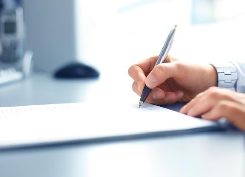 Businesswoman sitting at office desk signing a contract with shallow focus on signature.