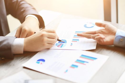 Image of human hands with pens pointing at business document at meeting