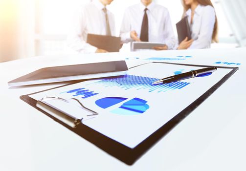 Close-up of business document in touchpad lying on the desk, office workers interacting in the background