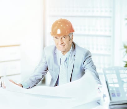 Portrait of professional architect with blueprints sitting behind table