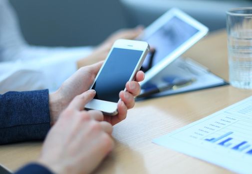 Smartphone handheld in closeup, colleagues working in background.