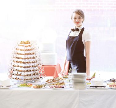 Young beautiful waitress girl on the background of a served table