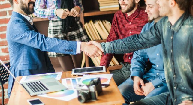 handshake business partners at a meeting in creative office on the background of business team