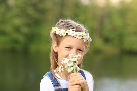 little girl in a wreath with a bouquet of flowers near the river in the Park on a Sunny day