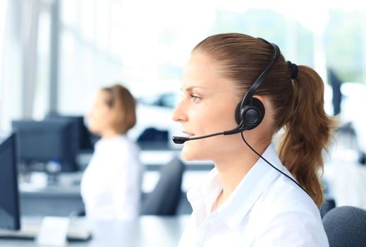 Beautiful young female call center operator with headset in office