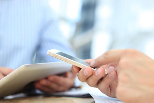 Smartphone, touchpad handheld in closeup, colleagues working in background.