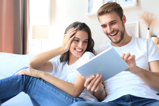 Young couple watching media content online in a tablet sitting on a sofa in the living room