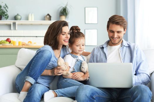 Father, mother and daughter using electronic devices sitting on sofa at living room