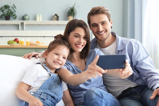 Beautiful young family with little child taking a selfie with a smartphone at home on the couch