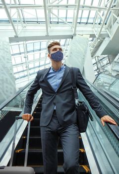 Businessman in protective mask at the airport going down the escalator