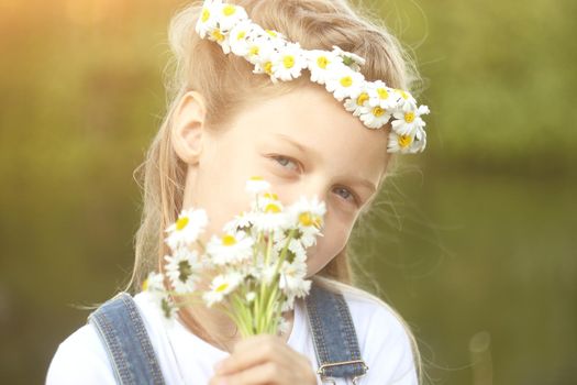 little girl in a wreath of daisies and a bouquet of flowers in the Park on a Sunny day