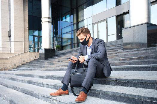 Modern man in formalwear and ptotective mask waiting job interview while sitting on the stairs outdoor