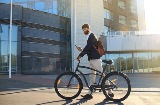 Young businessman in protective mask with bicycle and smartphone on city street