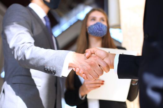 Business people in protective masks shaking hands, finishing up a meeting