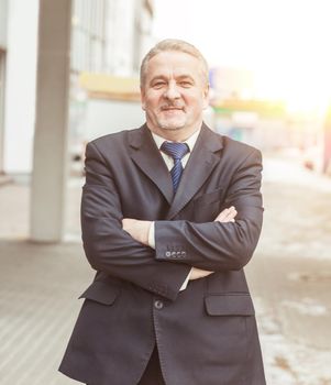 portrait of a successful businessman standing with crossed hands in front of him, on the background of office building