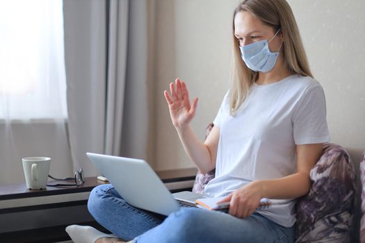Young woman in medical mask works from home during self isolation and quarantine. Work online and stay at home. Coronavirus outbreak, flu epidemic and covid-19