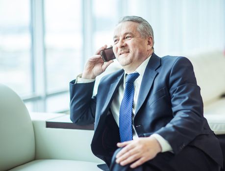 experienced businessman talking on smartphone sitting on couch in the office.