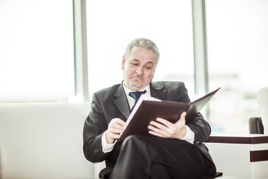 experienced lawyer reviews the documents with the terms of a new contract sitting on the sofa in the private office.
