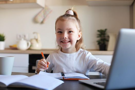 Smiling little girl handwrite study online using laptop at home, cute happy small child take Internet web lesson or class on PC