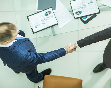 handshake business partners near the desktop, with the financial schedules.