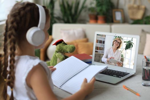 Distance learning. Cheerful little girl girl in headphones using laptop studying through online e-learning system