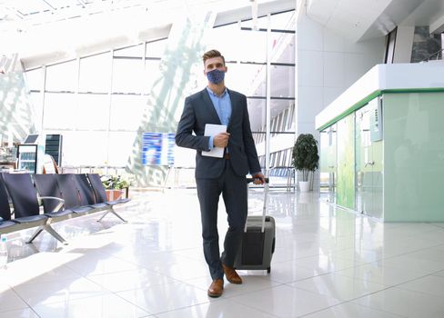Businessman in protective mask with suitcase in hall of airport. Airport in the coronavirus epidemic