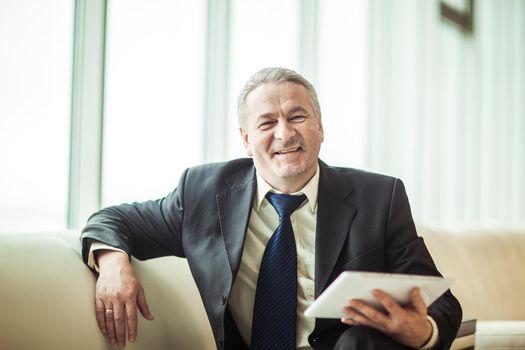 smiling businessman with digital tablet sitting on sofa in the office