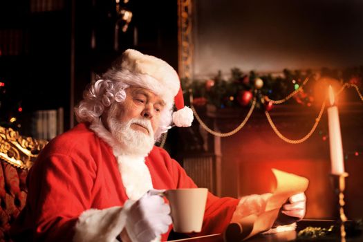 Portrait of happy Santa Claus sitting at his room at home near Christmas tree and reading Christmas letter or wish list.