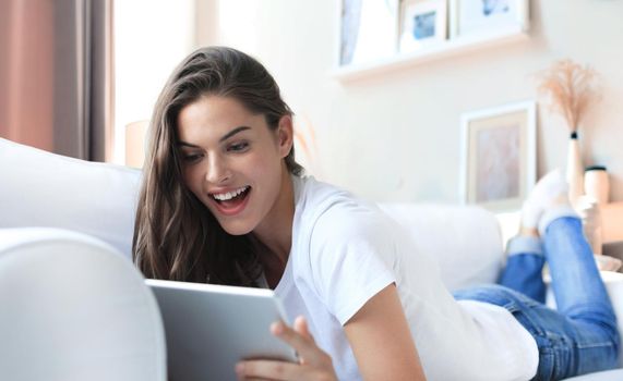 Beautiful young woman using tablet sitting on sofa at home at living room