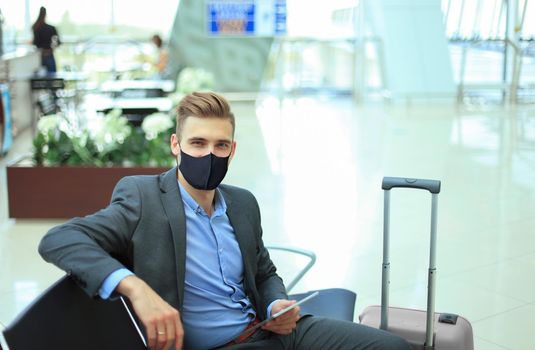 Businessman in protective mask with suitcase in hall of airport. Airport in the coronavirus epidemic