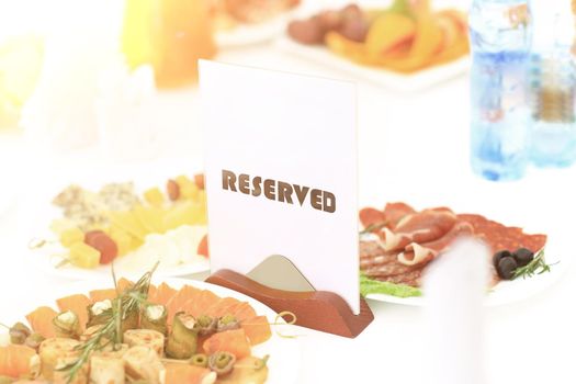 A reserved sign the restaurant table in bright sunny weather against a background of dishes