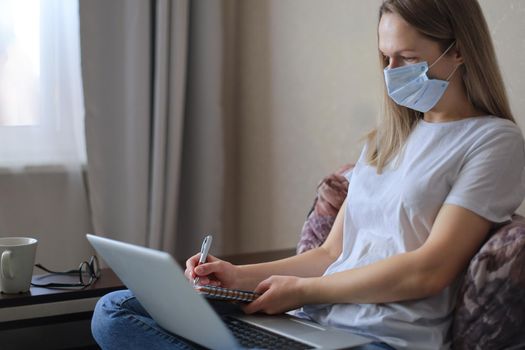 Young woman in medical mask works from home during self isolation and quarantine. Work online and stay at home. Coronavirus outbreak, flu epidemic and covid-19