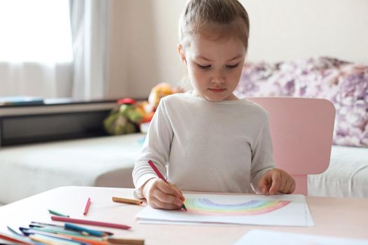 Girl painting rainbow at home, a symbol of UK National Health Service (NHS). Thanks to the doctors for their work. Stay at home Social media campaign