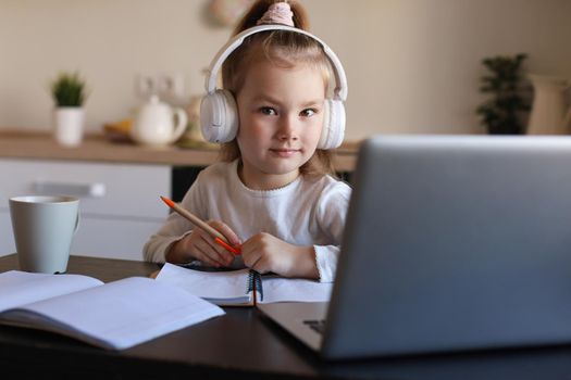 Smiling little girl in headphones handwrite study online using laptop at home, cute happy small child in earphones take Internet web lesson or class on PC