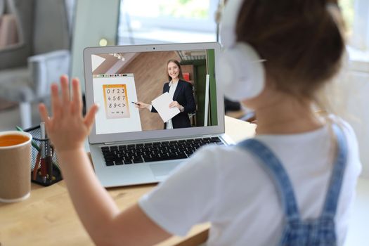 Distance learning. Cheerful little girl girl in headphones using laptop studying through online e-learning system