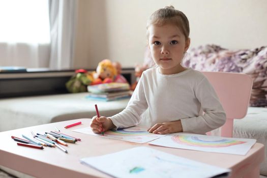 Girl painting rainbow at home, a symbol of UK National Health Service (NHS). Thanks to the doctors for their work. Stay at home Social media campaign