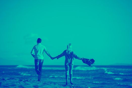 Young couple having fun walking and hugging on beach during autumn sunny day