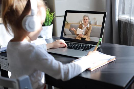 Distance learning. Cheerful little girl girl in headphones using laptop studying through online e-learning system