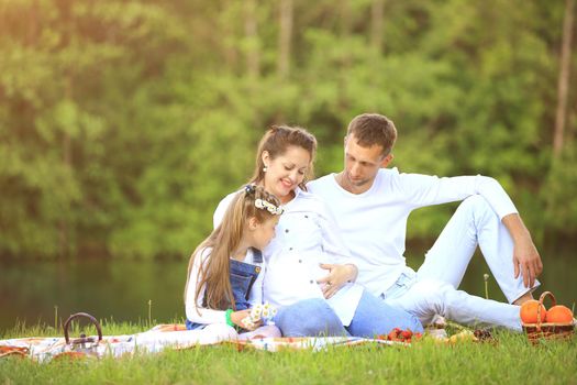 pregnant mother and happy father and little daughter at a picnic in the Park on a Sunny day. the photo has a empty space for your text