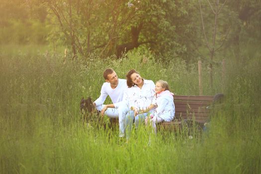 A pregnant woman with her daughter and husband in a park on a bench communicate with each other