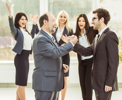 handshake of business partners on background of cheering business team .the photo has a empty space for your text