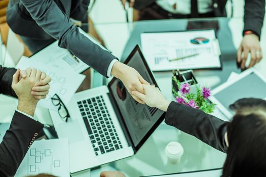 handshake of business partners on the background of financial graphs lying in the workplace