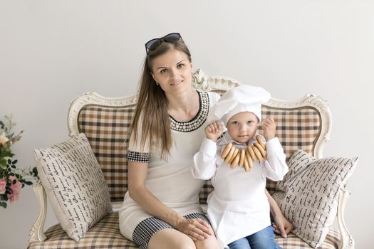 Portrait of a happy mother and her young child in the form of a cook on the couch
