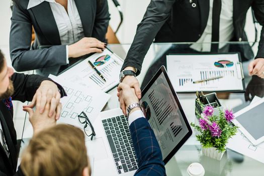 handshake of business partners on the background of financial graphs lying in the workplace
