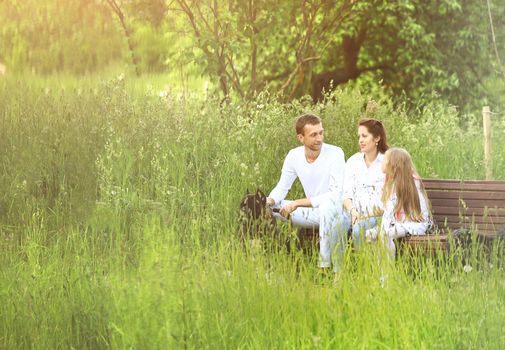 little girl with parents sits on a Park bench in summer Sunny day.the photo has a space for your text.